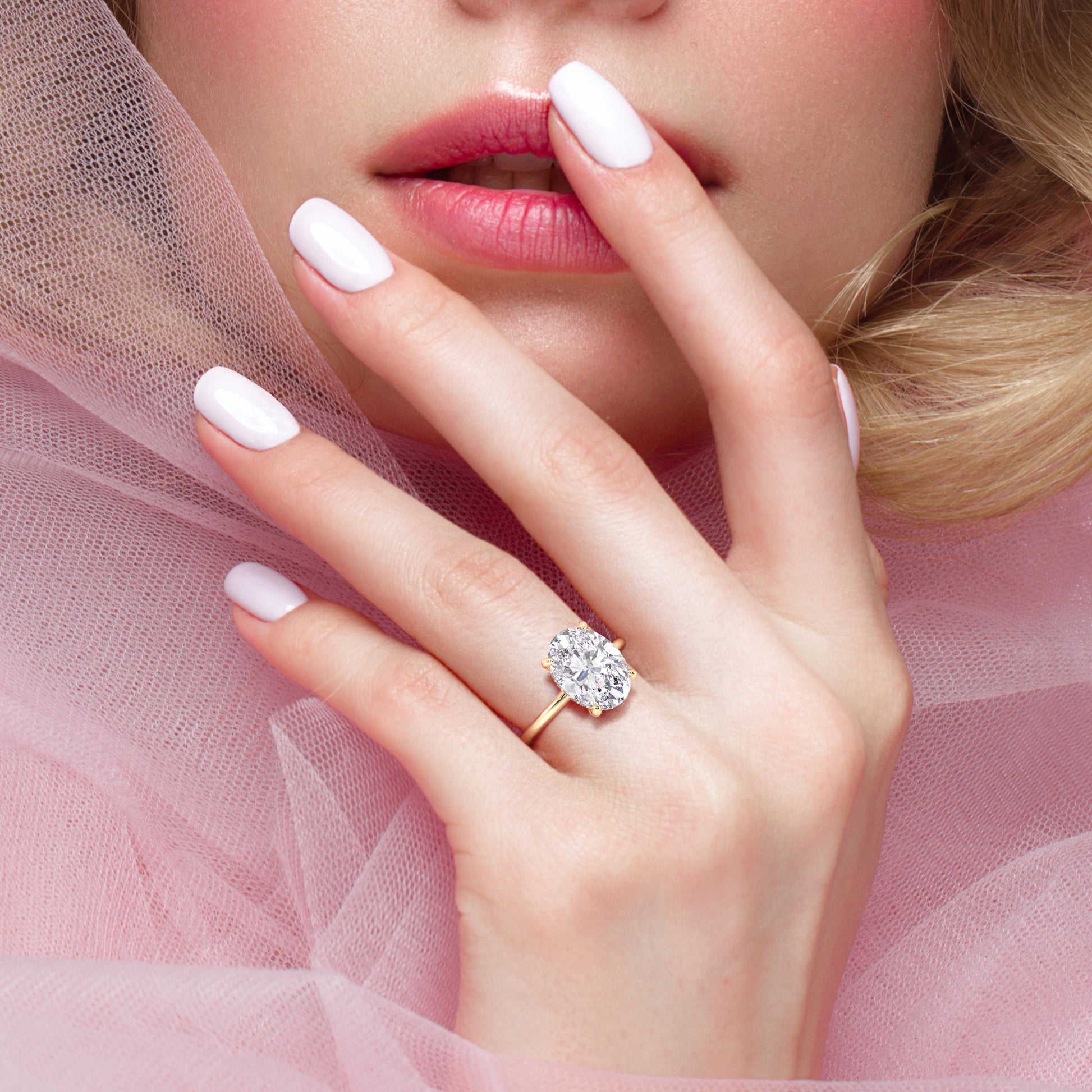 Elegant oval diamond engagement ring in 14K or 18K gold, showcased on model's finger against soft pink background.|
#14KRecycledYellowGold 
#18KRecycledYellowGold