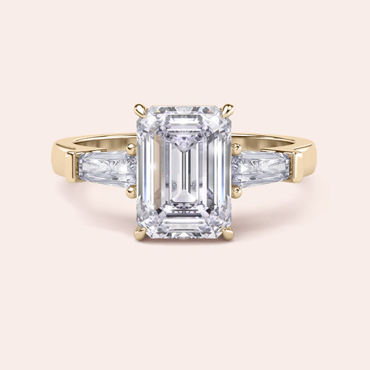 Yellow gold engagement ring featuring a prominent emerald-cut diamond, flanked by smaller diamonds on a delicate band, exuding luxury.