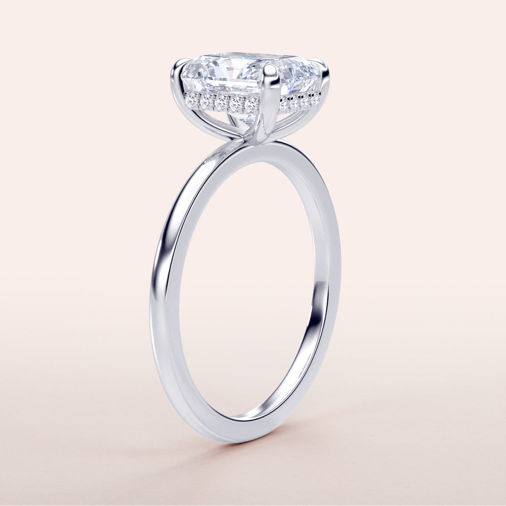 Close-up of a radiant hidden halo engagement ring in white gold, featuring an emerald-cut diamond. Available in 14K, 18K, or platinum.|
#14KRecycledWhiteGold
#18KRecycledWhiteGold
#Platinum
