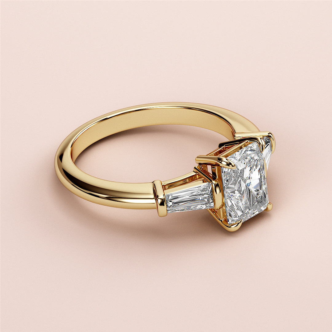 Elegant 14K or 18K gold engagement ring featuring a radiant-cut diamond center stone with tapered baguettes. Not worn on model.|
#14KRecycledYellowGold
#18KRecycledYellowGold