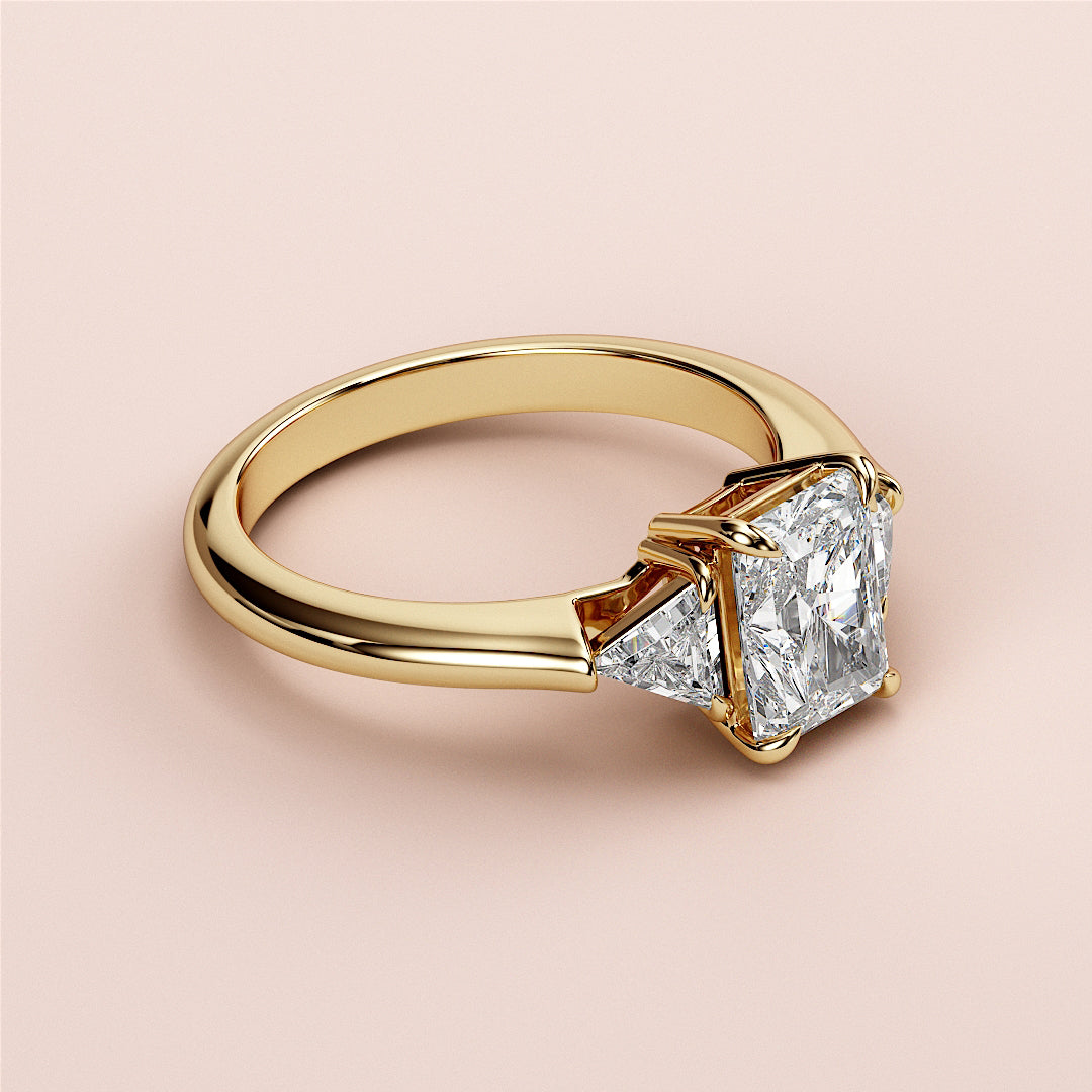 Elegant 14K gold engagement ring featuring a radiant-cut diamond with two triangular side diamonds in a stunning design.|
#14KRecycledYellowGold
#18KRecycledYellowGold