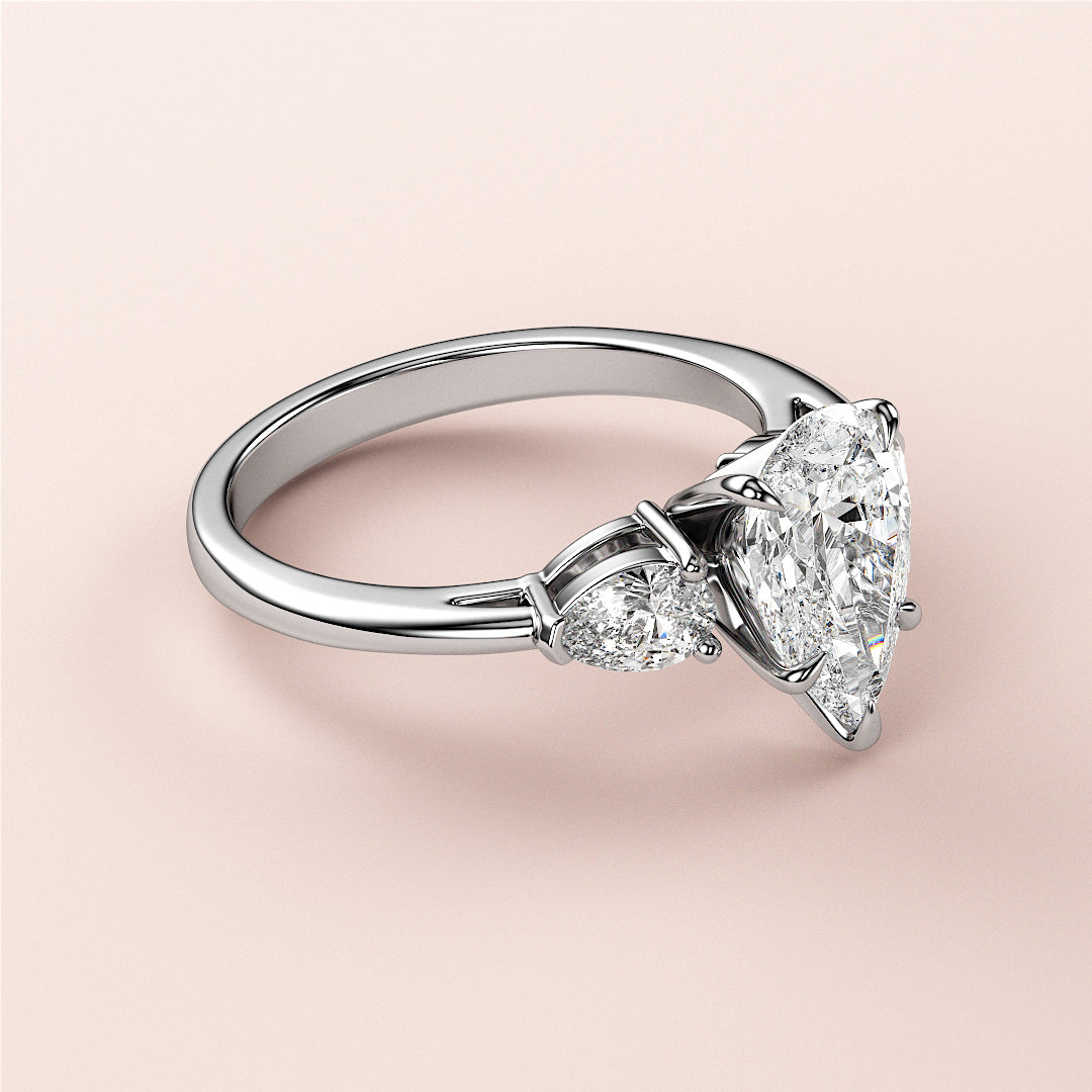 Elegant 14K and 18K gold engagement ring with a pear-shaped diamond centerpiece and two smaller diamonds on a sleek band.|
#14KRecycledWhiteGold
#18KRecycledWhiteGold
#Platinum