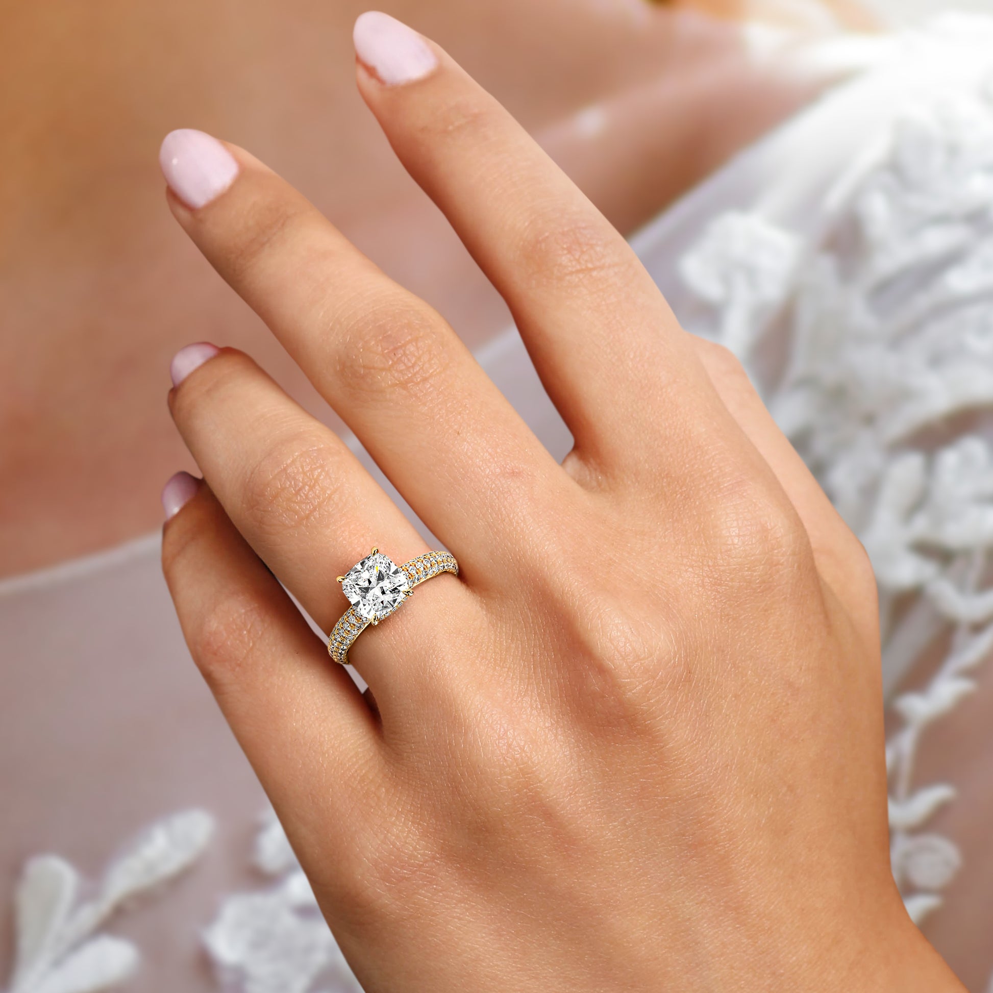 Elegant cushion-cut diamond engagement ring in 14K or 18K gold, or platinum, set in a pave band, worn on a model's hand.|
#14KRecycledYellowGold
#18KRecycledYellowGold