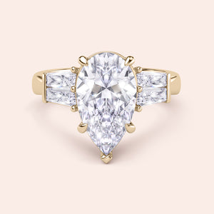Pear shaped diamond engagement ring in yellow gold with tapered baguette side stones, classic three stone design with brilliant center diamond 