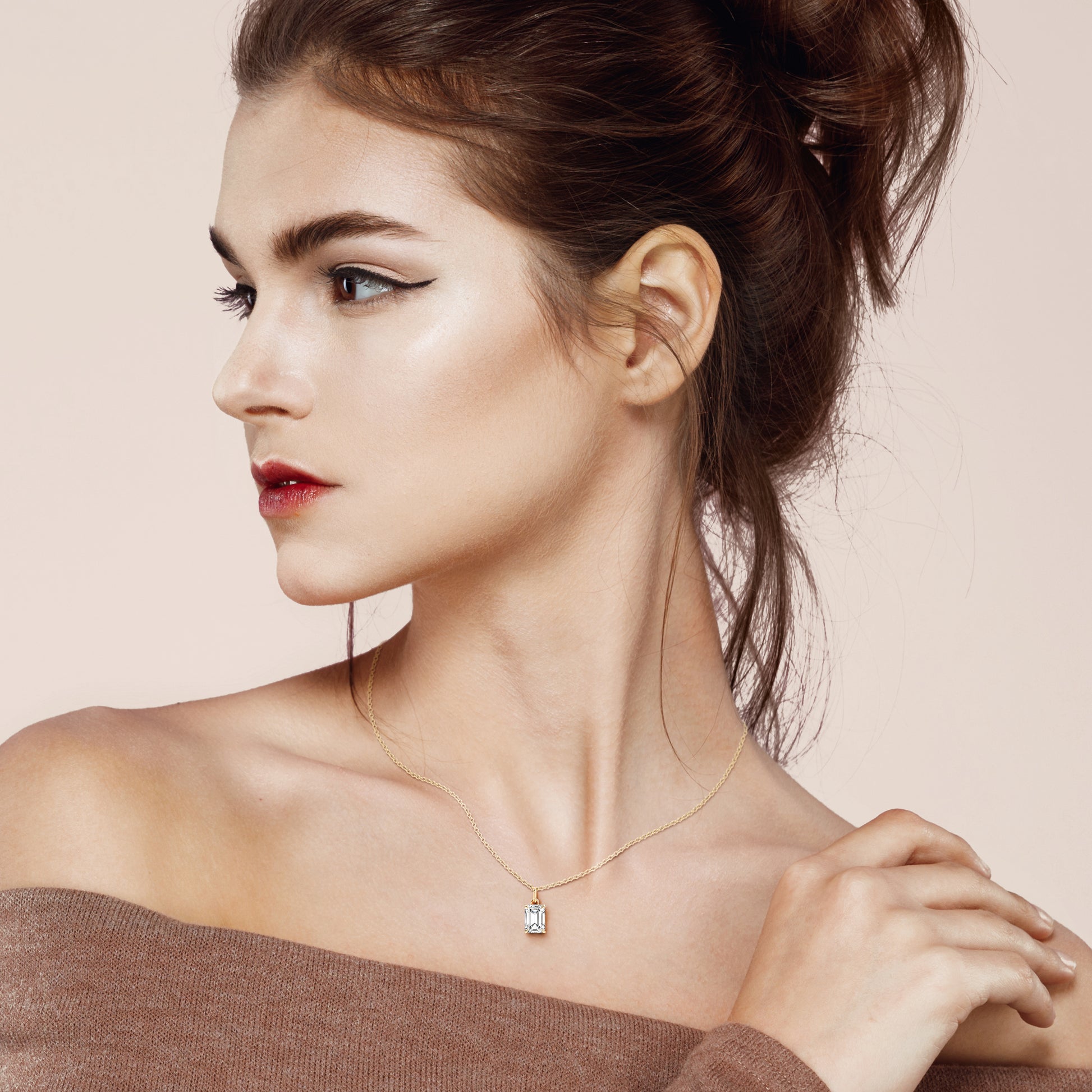 A stunning woman wearing an emerald-cut solitaire diamond pendant in a four-prong yellow gold setting. The refined design highlights the clean lines of the emerald-cut diamond, making it a sophisticated piece for both everyday wear and special occasions.
| #14KRecycledYellowGold #18KRecycledYellowGold

