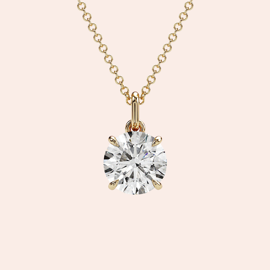 A close-up of a solitaire round-cut diamond pendant in a four-prong yellow gold setting. The brilliant diamond is enhanced by the warm tones of the gold, creating a classic and radiant look.
