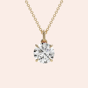 A close-up of a solitaire round-cut diamond pendant in a four-prong yellow gold setting. The brilliant diamond is enhanced by the warm tones of the gold, creating a classic and radiant look.
