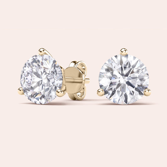 Luxurious 3-Prong Martini Diamond Earrings in yellow gold, isolated on beige background 