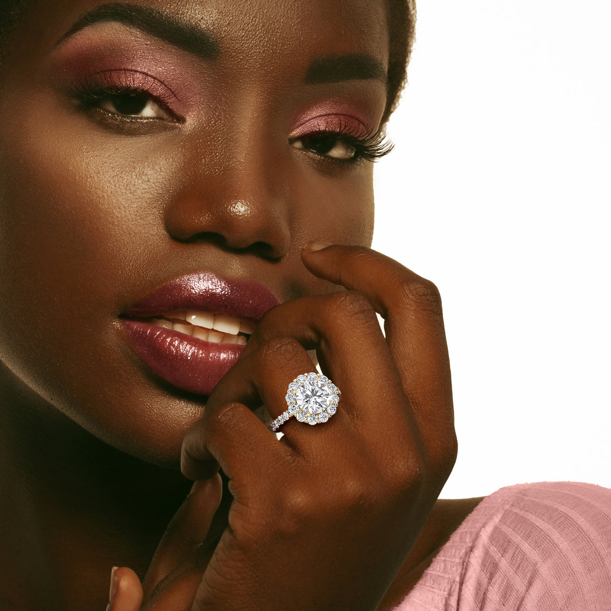 Round brilliant diamond halo ring on model's hand, available in 14K, 18K gold or platinum. Perfect for elegant sophistication.