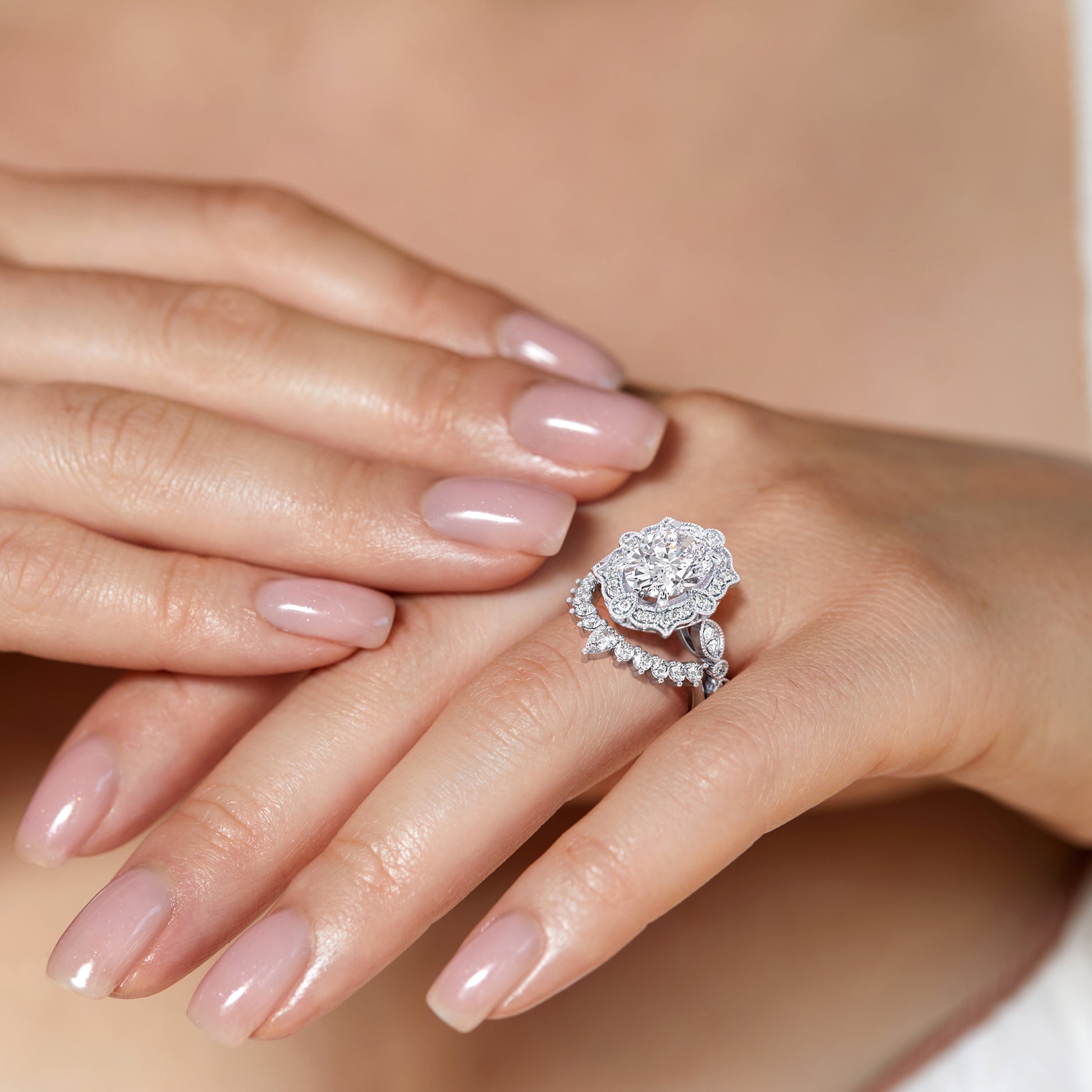 Hands elegantly displaying vintage-inspired oval halo diamond ring set featuring delicate filigree details in recycled white gold | #14KRecycledWhiteGold #18KRecycledWhiteGold #Platinum