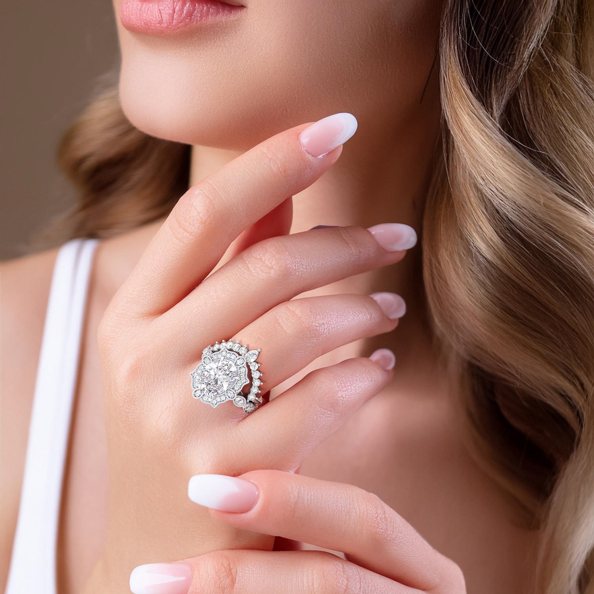 Close-up of woman gracefully showcasing oval halo diamond engagement ring set with detailed filigree accents in recycled white gold | #14KRecycledWhiteGold #18KRecycledWhiteGold #Platinum