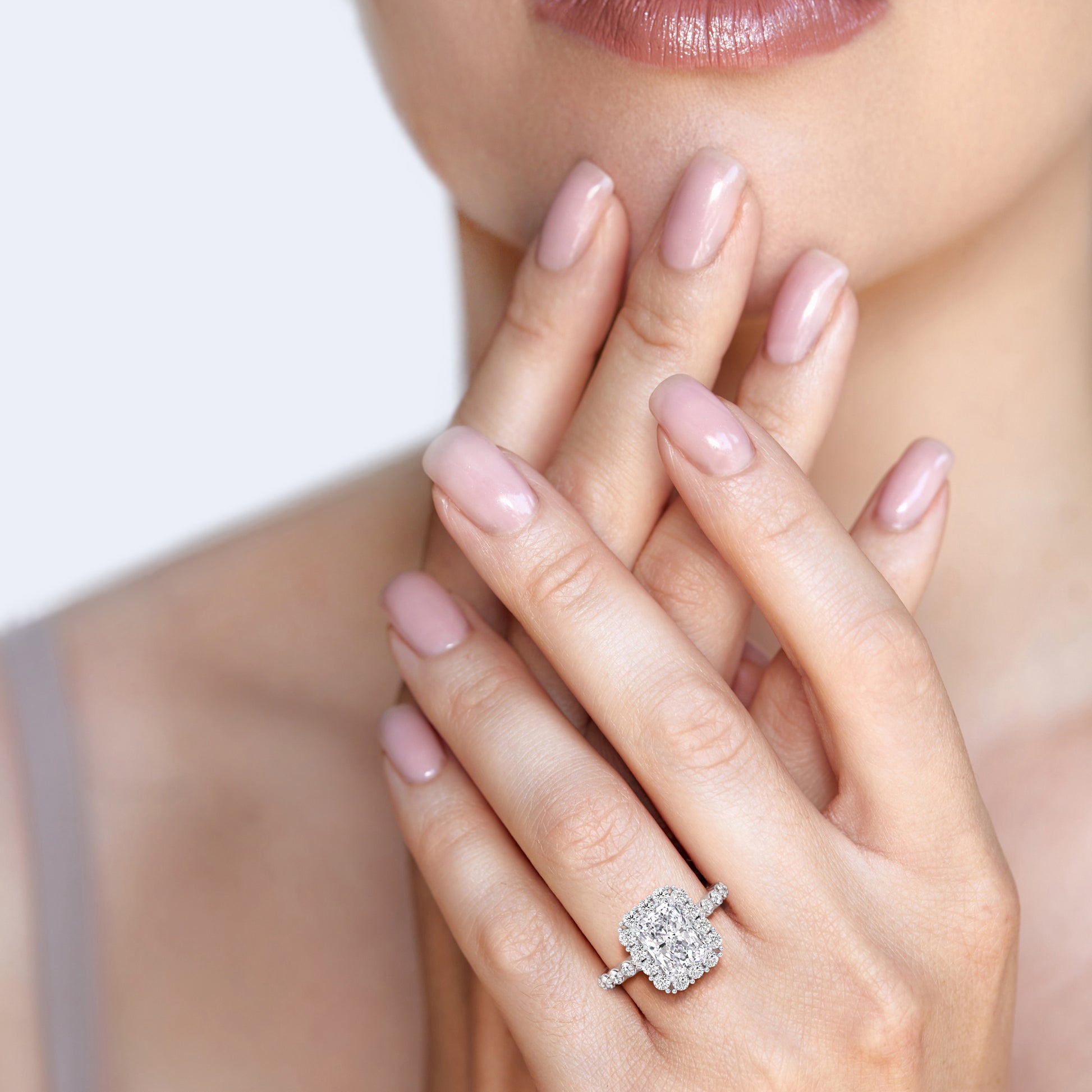 Elegant woman wearing radiant-cut diamond halo ring with sparkling diamond band in white gold or platinum | #14KRecycledWhiteGold #18KRecycledWhiteGold #Platinum