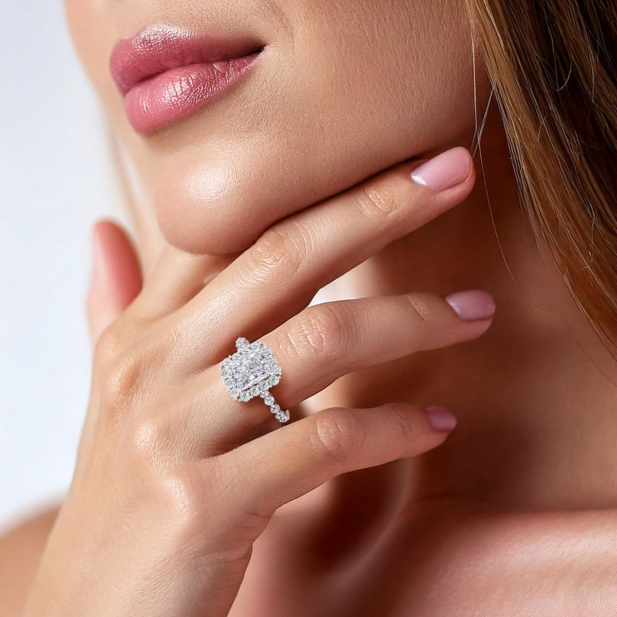 Beautifully styled woman wearing radiant-cut diamond engagement ring, accented with a sparkling halo and diamond band in white gold or platinum 