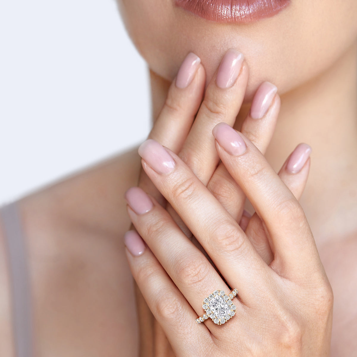 Elegant woman wearing radiant-cut diamond halo ring with sparkling diamond band in yellow gold 