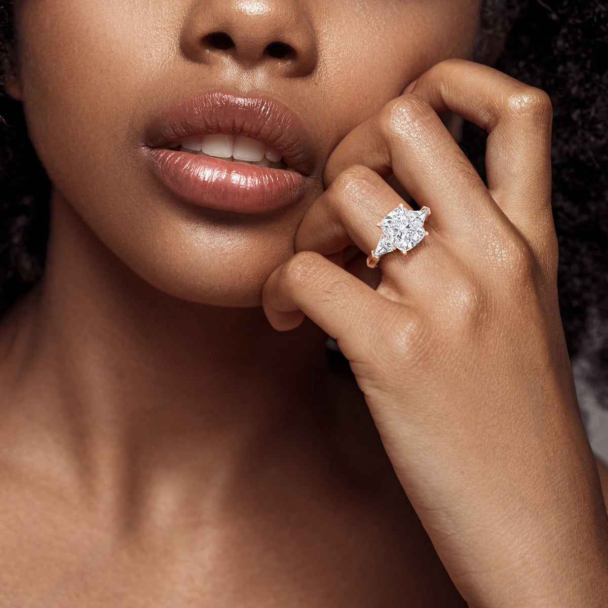 Woman wearing a stunning 14K or 18K Three stone Rose Gold engagement ring with a cushion-cut diamond, and shield side stones showcasing exceptional craftsmanship. 