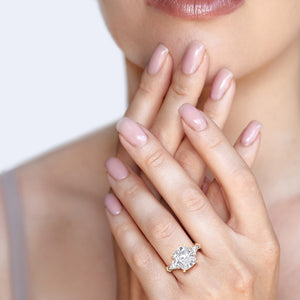 Womans hand showcasing a stunning 14K yellow gold three stone engagement ring with a cushion-cut diamond and shield shaped side stones. 