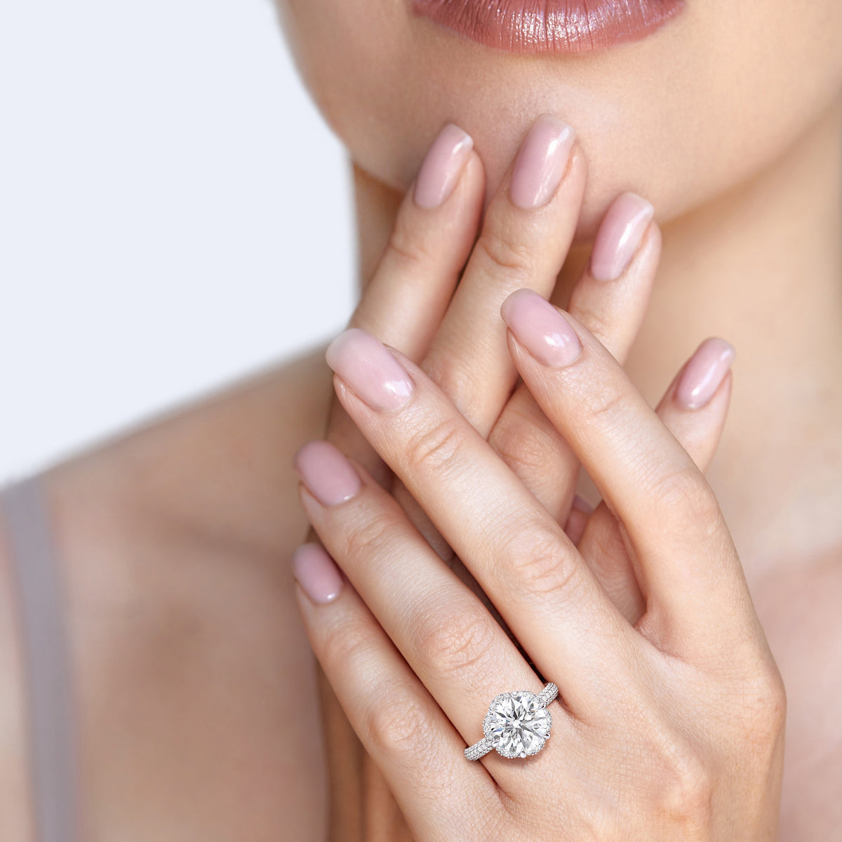 Elegant woman displaying a white gold cushion-cut diamond ring, emphasizing its luxurious double halo and diamond band, blending classic and contemporary styles. 