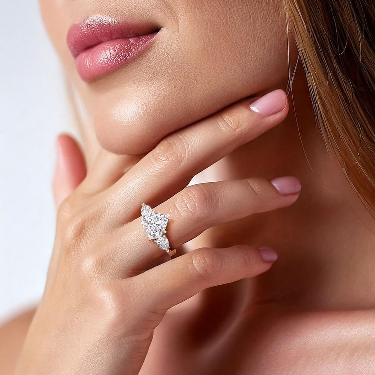 Close-up on a woman's hand adorned with a rose gold heart-shaped diamond ring, the teardrop side diamonds enhancing its allure. 