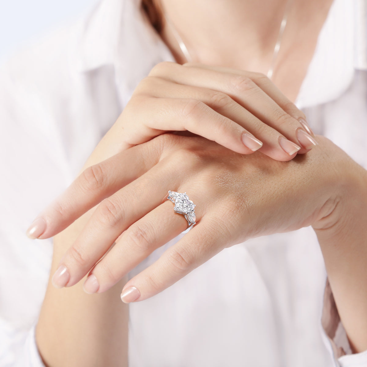 Elegant woman displaying a white gold heart-shaped diamond engagement ring, accentuated with teardrop side diamonds, blending classic romance with modern style. 