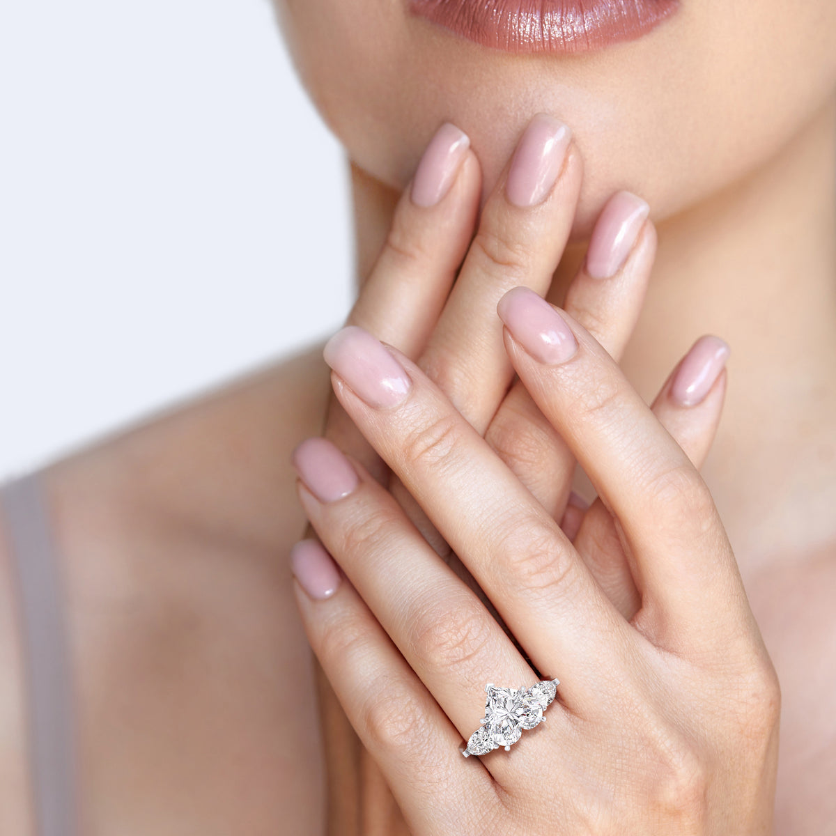 Close-up on a woman's hand adorned with a white gold heart-shaped diamond ring, the teardrop side diamonds enhancing its allure. 