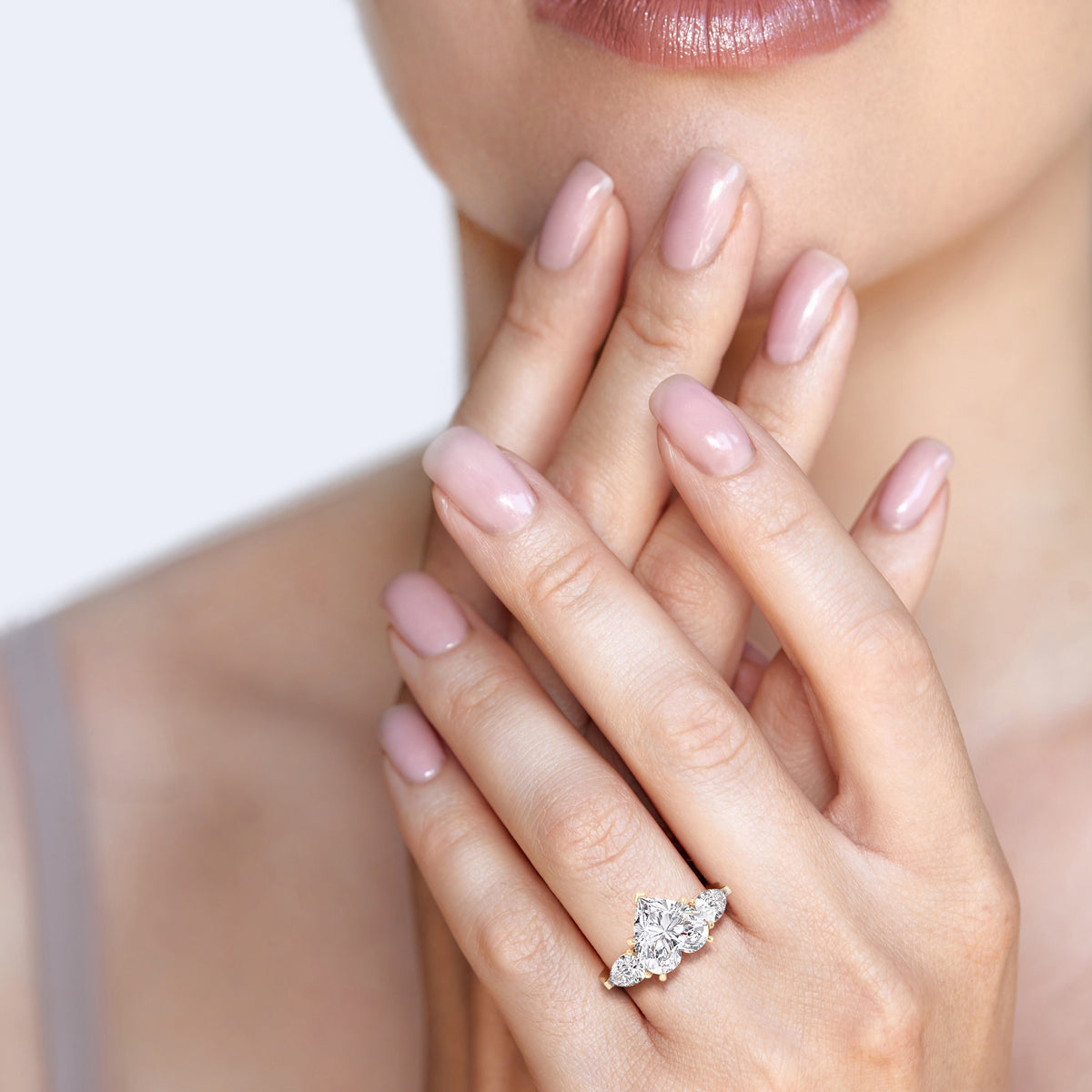 Close-up on a woman's hand adorned with a yellow gold heart-shaped diamond ring, the teardrop side diamonds enhancing its allure. 