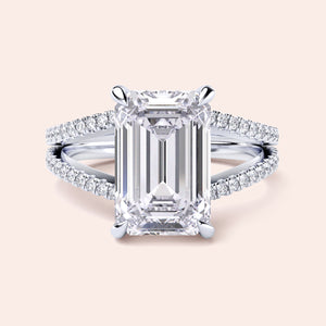 Close-up of an emerald-cut diamond engagement ring with split shank in 14K or 18K white gold, featuring aPave band.