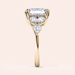 Elegant 14K gold engagement ring featuring asscher and pear-cut side stones in a floral design, set against a beige background.