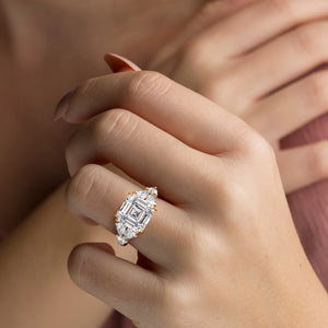 A model wearing a luxurious 14K/18K gold or platinum ring with an emerald-cut diamond and pear-shaped side stones.