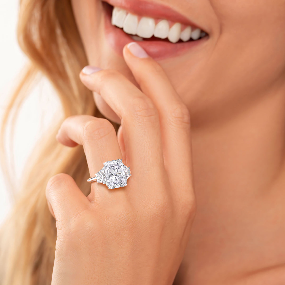 Woman wearing an elegant 14K, 18K, or platinum ring with a radiant-cut diamond in a sleek trapezoid design.
