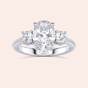 Elegant 14K or 18K gold three-stone engagement ring with oval center diamond and round side stones on aPave band.