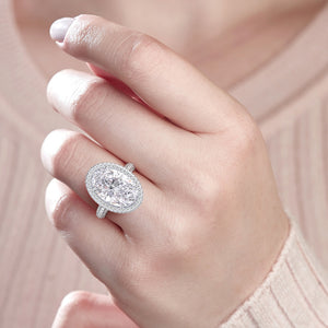Woman wearing an elegant oval-shaped diamond ring with halo setting in 14K or 18K gold, showcasing a dazzling central diamond.