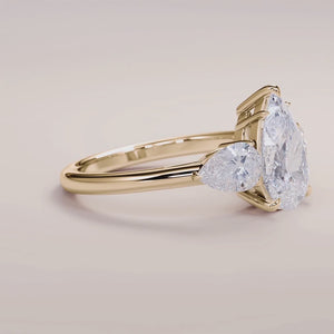 Elegant three-stone engagement ring in 14K or 18K yellow gold, featuring an oval diamond with pear side stones.