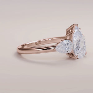 "Rose Gold 14K engagement ring featuring a pear three-stone design with side stones, perfect for timeless elegance.