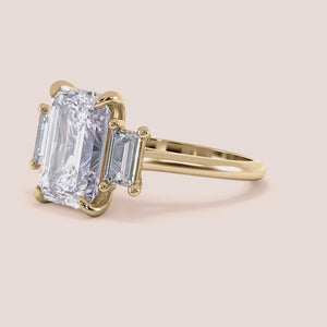 Radiant-cut diamond engagement ring with side stone accents in 14K yellow gold, displayed on a neutral background.