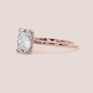 A stunning cushion-cut diamond engagement ring in 14K or 18K rose gold, featuring a delicate band and prominent centerpiece.
