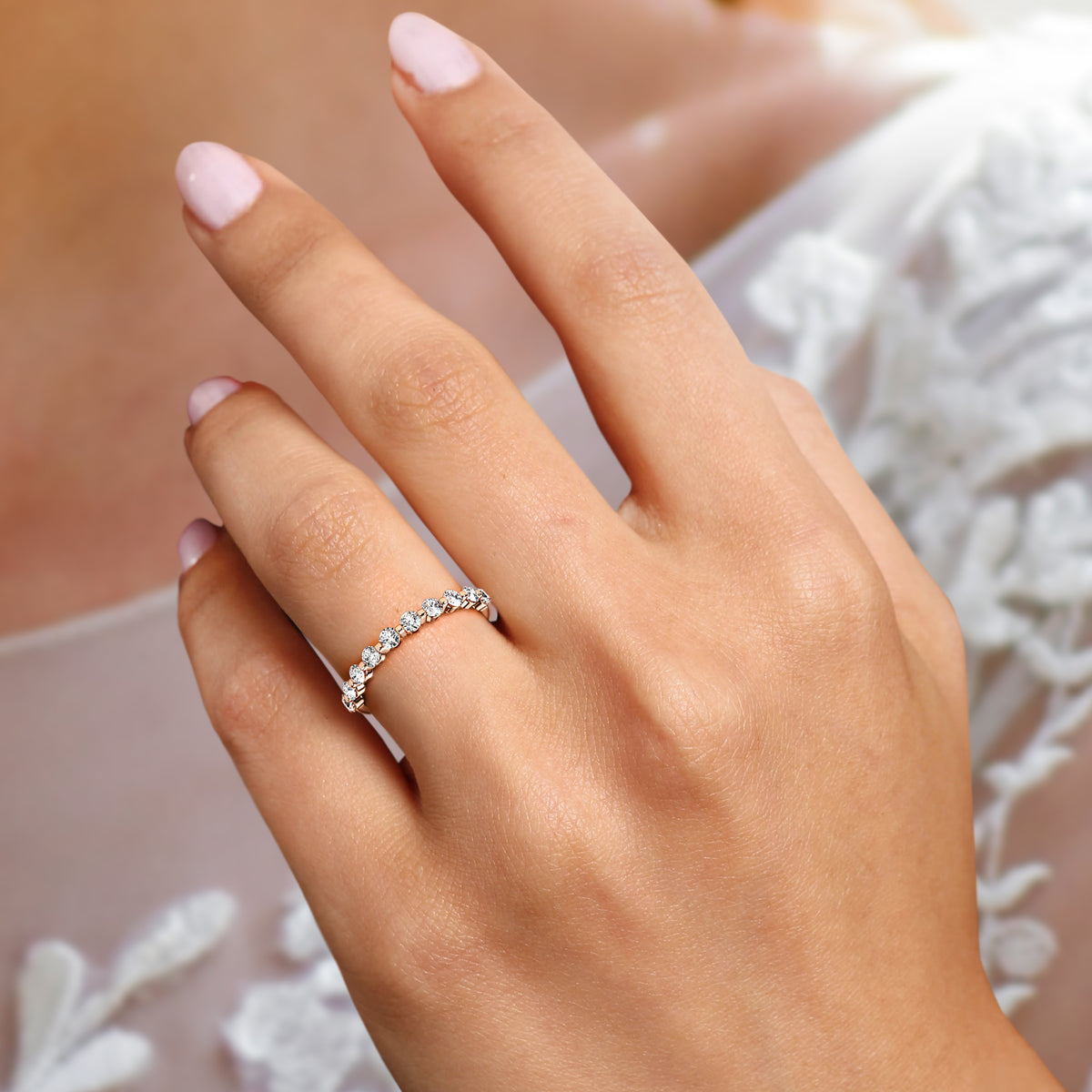 Woman wearing a delicate 14K or 18K rose gold diamond eternity band, featuring round brilliant-cut diamonds, showcasing elegance. 