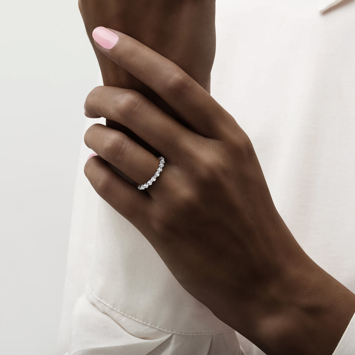 Elegant diamond eternity band with round cut diamonds in 14K/18K white gold or platinum, worn on a model's finger. 