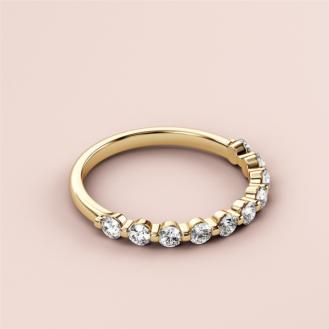 Elegant 14K gold wedding band featuring a row of round brilliant-cut diamonds on a soft pink background. 