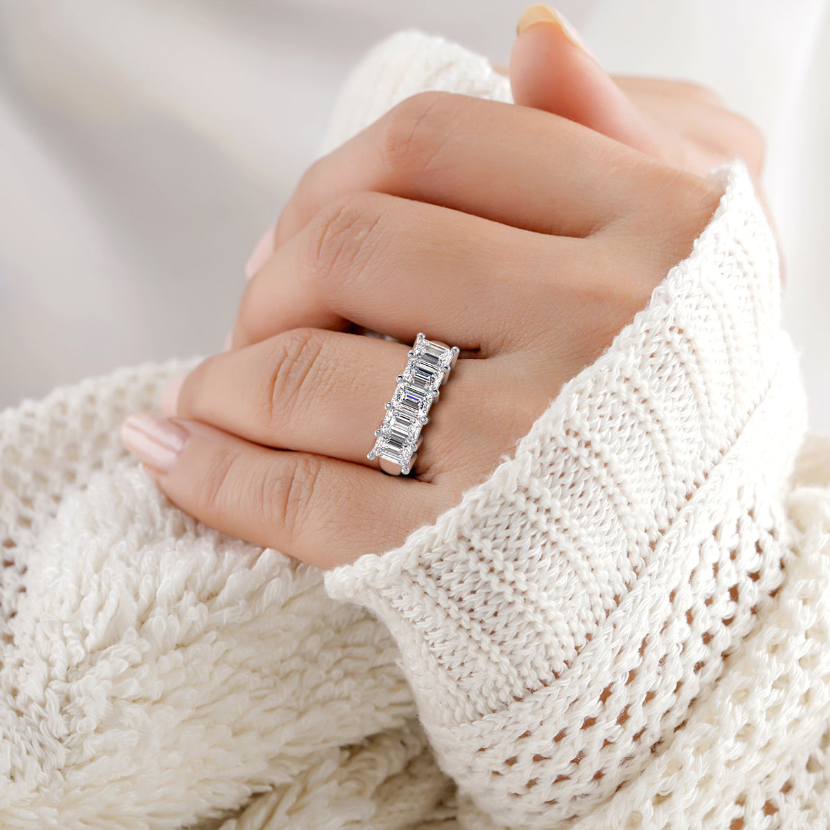Woman wearing a luxurious 14K white gold five-stone emerald cut eternity band, showcasing exquisite craftsmanship on a soft pink background. 