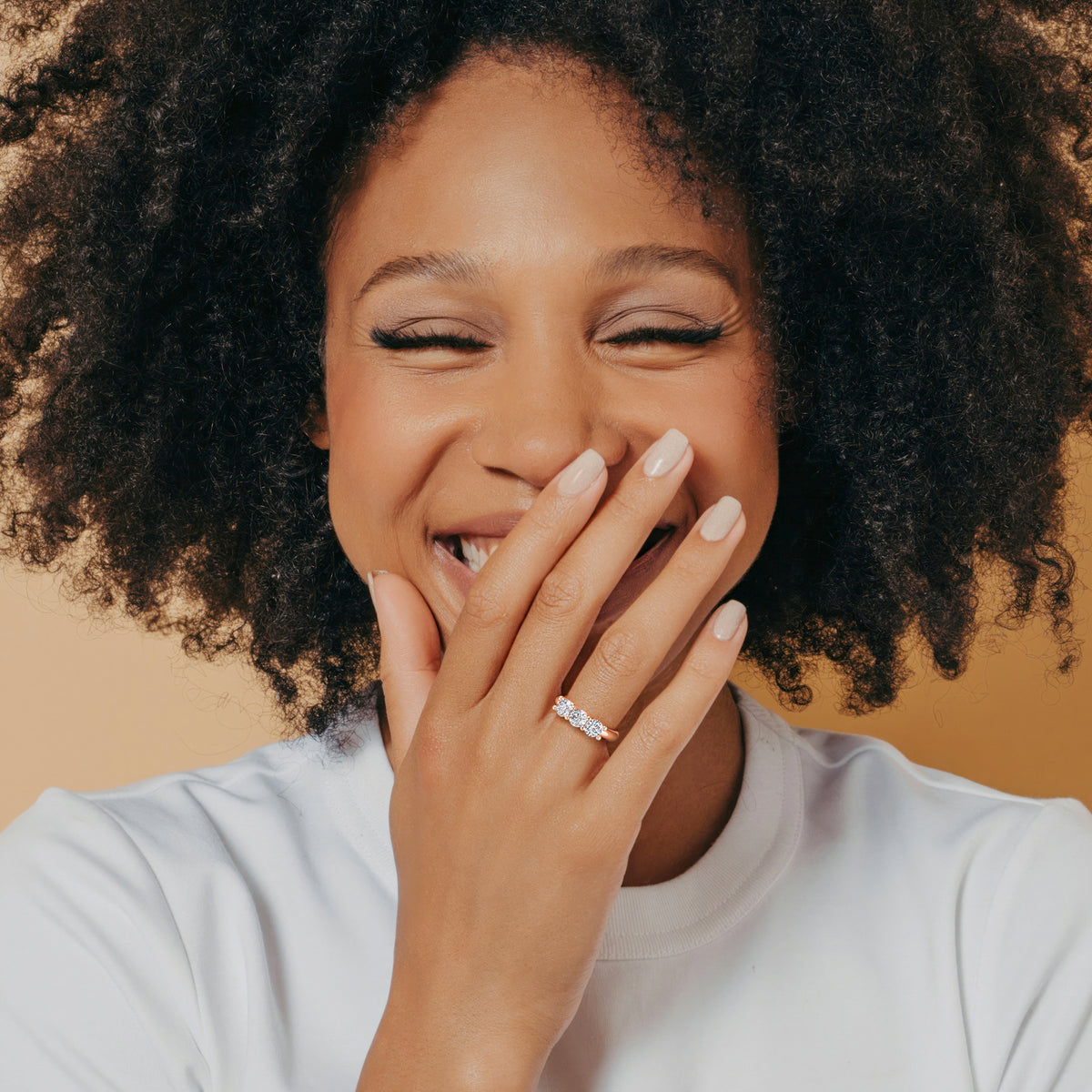 Elegant three-stone diamond engagement ring in 14K rose gold, featuring cushion-cut centerpiece and round side stones, worn on model. 