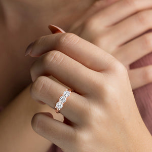 Elegant 14K rose gold three-stone wedding band with round brilliant diamonds worn on model's hand, perfect for eternity moments. 