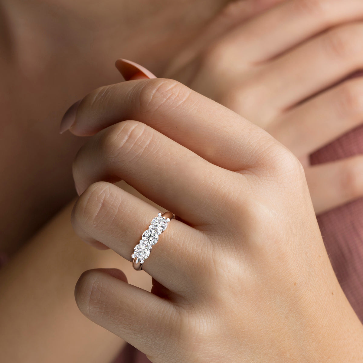 Close-up of a woman wearing a stunning 14K or 18K gold three-stone wedding band, showcasing radiant diamonds in a U-prong setting. 