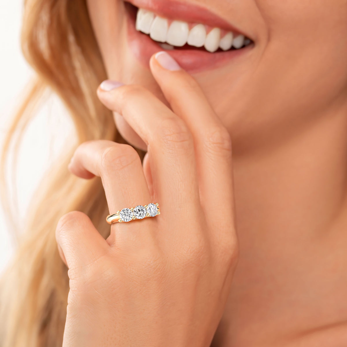 Elegant three-stone diamond ring in 14K yellow gold, featuring round brilliant-cut diamonds, worn on a model's hand. 