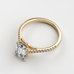 Close-up of a stunning 14K and 18K yellow gold engagement ring featuring an Asscher-cut emerald and delicate diamonds.