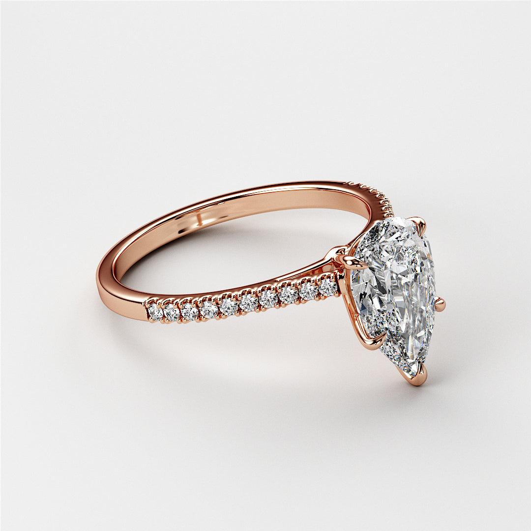 Pear-shaped diamond engagement ring in rose gold, featuring a delicate diamond-studded band. Available in 14K, 18K, and platinum.
