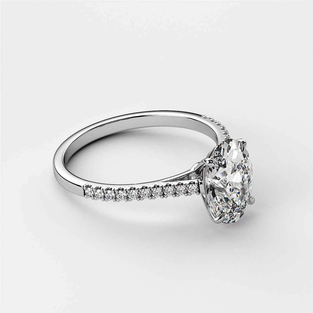 Close-up of a white gold oval solitaire engagement ring with pave detailing, featuring a pear-shaped diamond. Available in 14K, 18K, or platinum.