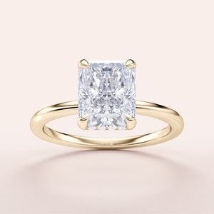 Radiant-cut diamond engagement ring in 14K or 18K gold, showcasing hidden halo design, on light beige background.