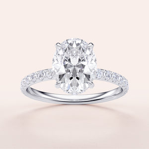 Elegant oval diamond engagement ring in 14K or 18K gold or platinum with a delicate pave band, set against a light background.