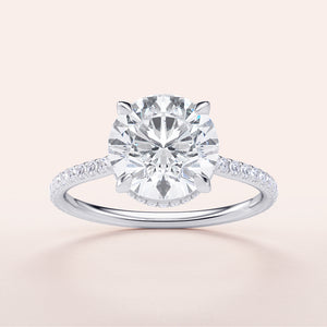 Round diamond engagement ring in 14K or 18K white gold, featuring a delicate pave band and a hidden halo design.