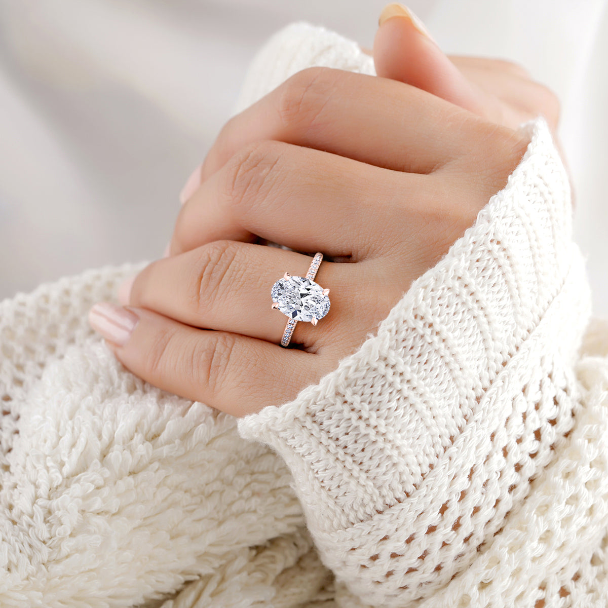 Elegant diamond oval ring in 14K or 18K rose gold, worn on model's hand with a cozy white sweater background.